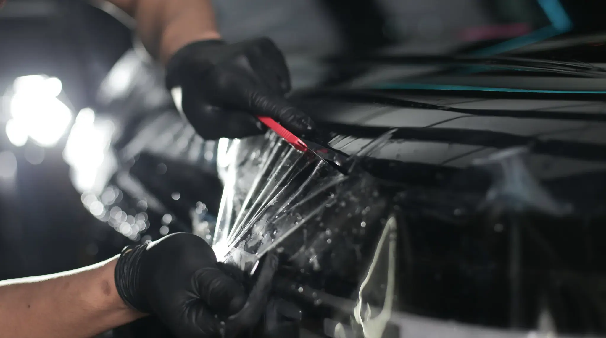 QUAD Film installer hand cutting film beside a car panel edge