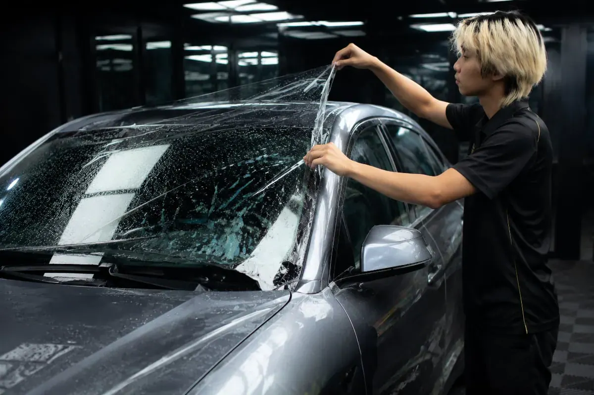 Juruteknik memasang filem pelindung cermin hadapan TPU jernih pada cermin kereta